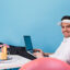 man in glasses and cap works on isolated background. guy posing with laptop, cocktail and inflatable circle.